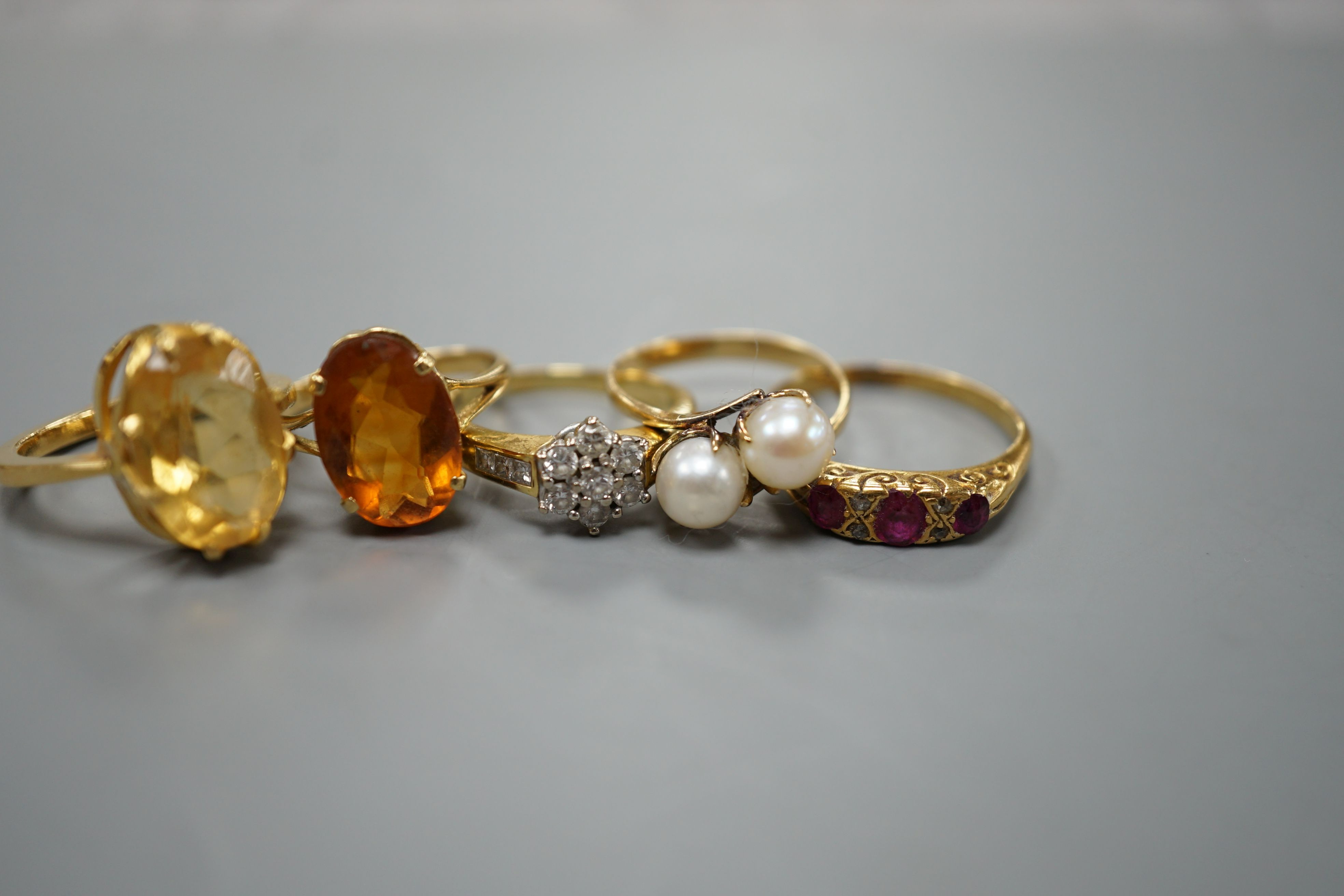 Five assorted gold and gold coloured metal dress rings, comprising a two stone cultured pearl stamped 18k, size L, an 18ct gold diamond cluster, size L, an unmarked citrine?, an 18ct orange stone, size L and an early 20t